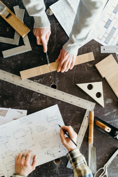 Woodworkers working on a table with drawings and measurements.