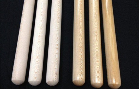 Six wooden broom and mop handles with a clear lacquer finish and tinted maple stain, available in bulk.