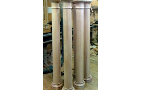 Four tall wooden columns featuring a tapered middle section, complete with capitals and bases.