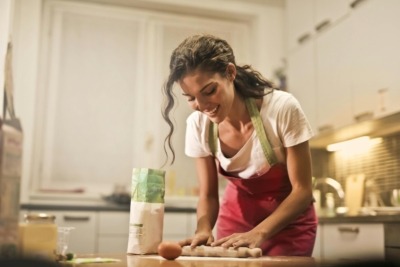 A woman uses a wood rolling pin in the kitchen while baking.