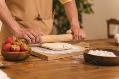 A man using a wood rolling pin to flatten dough.