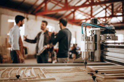 A wood CNC machine that is used for CNC machining services, with three people standing and talking in the background.