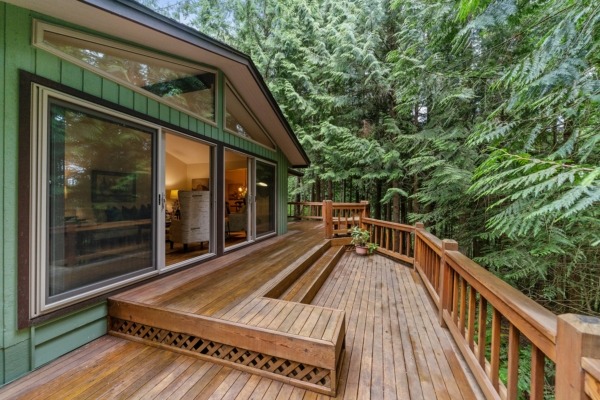 A wood deck at the back of a home in the woods.